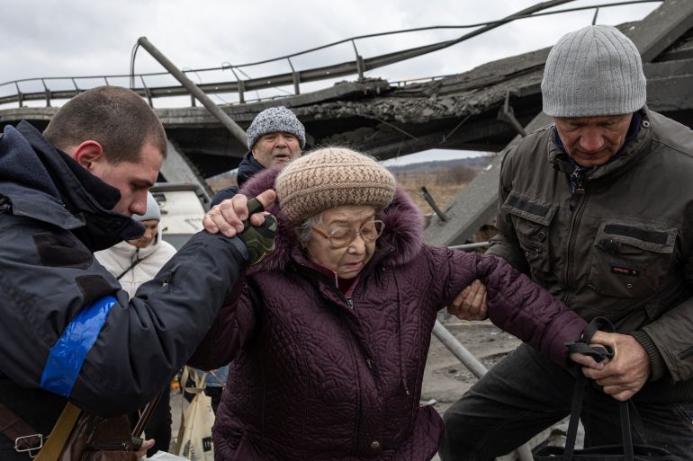 Люди помогают женщине перейти разрушенный мост в городе Ирбин под Киевом, Украина.